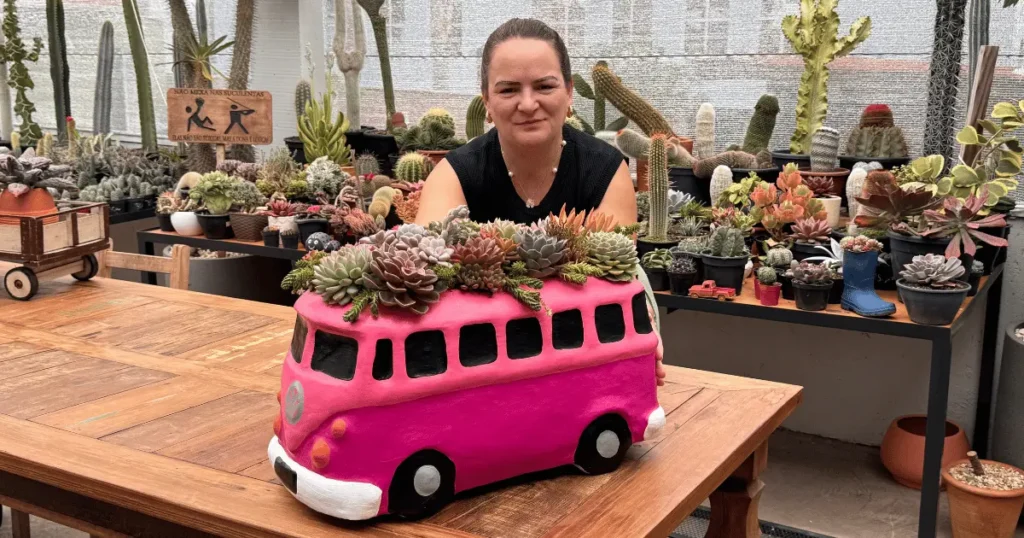 Mulher em estufa de cactos e suculentas com arranjo criativo em vaso no formato de kombi rosa, destacando o cultivo criativo de suculentas